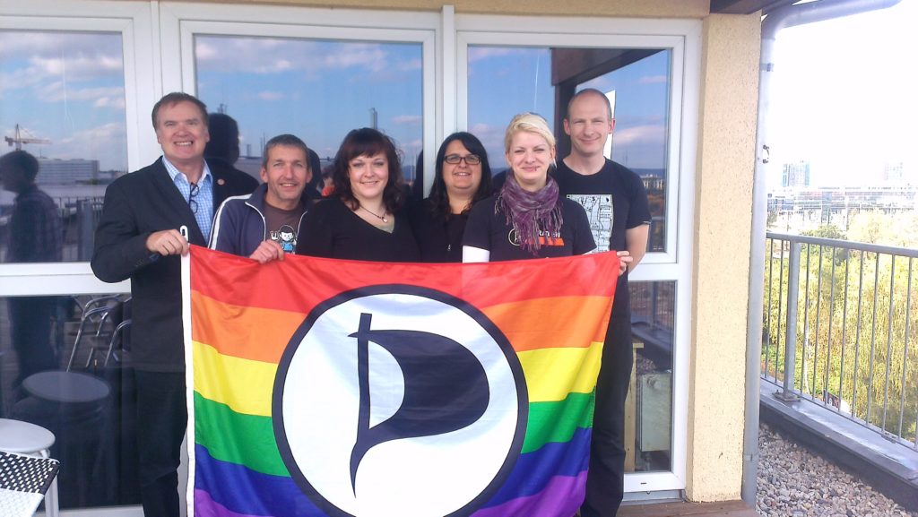 der neue Vorstand ist zu sehen mit der Queeratenflagge in der Hand