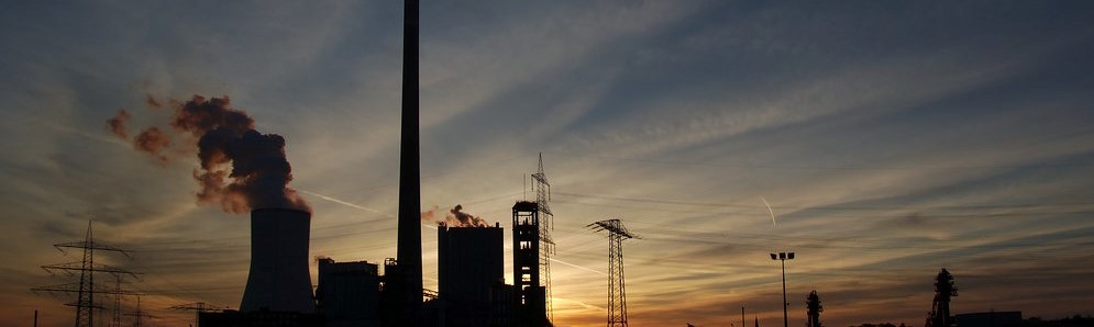 Das Bild zeigt eine rauchendes Kraftwerk vor einer untergehenden Sonne.