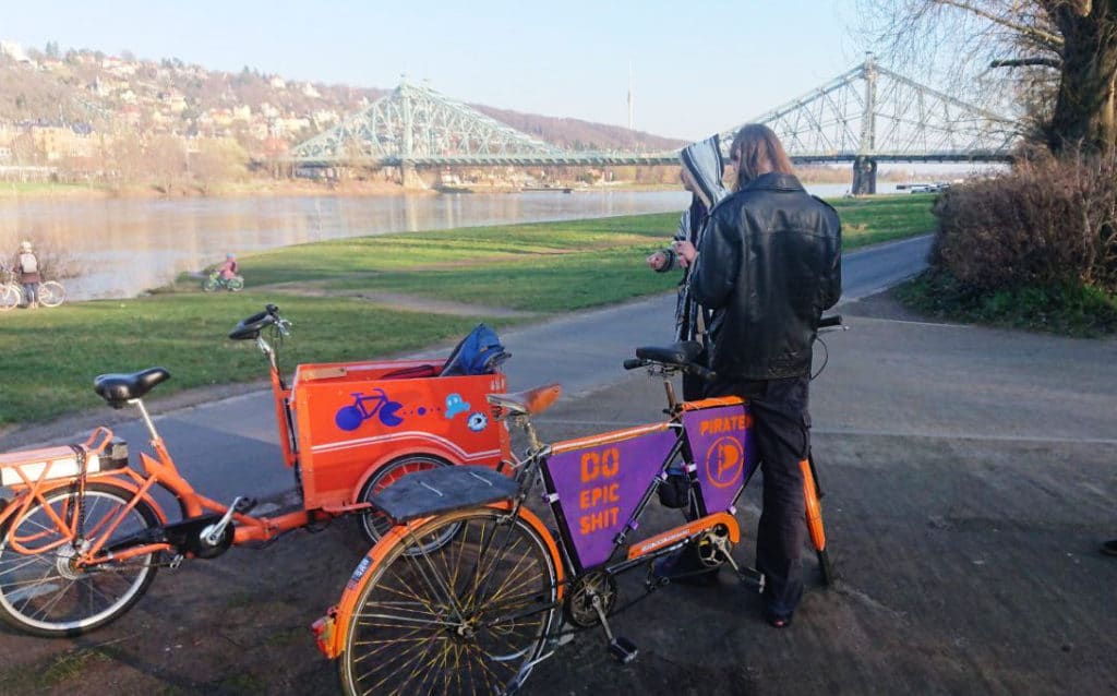 Ein Oranges Lastenrad und Tandem mit Piratenaufschrift vor dem Blauen Wunder..