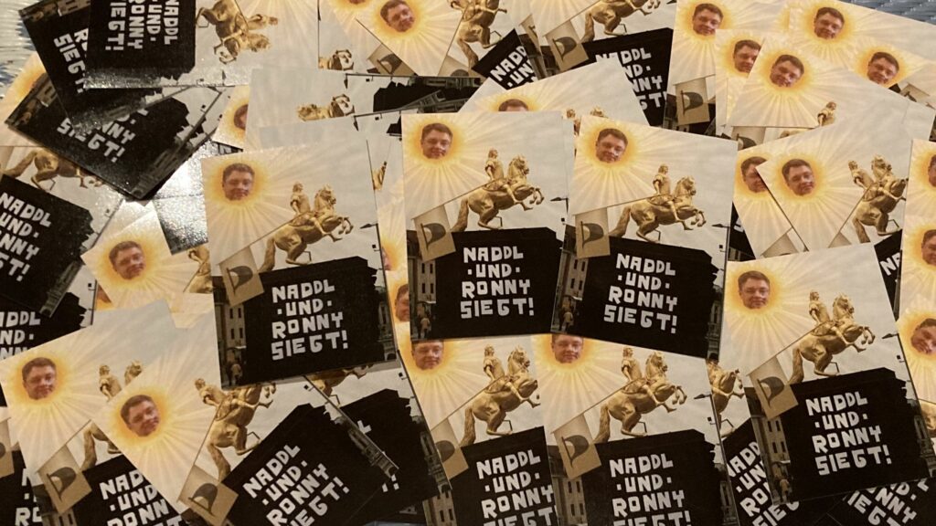 Viele Sticker mit dem Bild des goldenen Reiters, auf dessen Sockel der Schriftzug "Naddl & Ronny" zu sehen ist. Holger Zastrow ist als traurige "Teletubby-Sonne" oben links zu sehen.